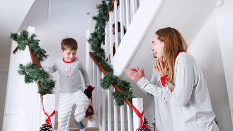 Los-padres-saludo-emocionado-a-niños-vistiendo-pijamas-bajando-escaleras-con-medias-en-la-mañana-de-Navidad