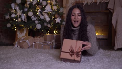 Das-Mädchen-öffnet-die-Box-mit-einem-Geschenk-und-freut-sich-auf-den-Boden-neben-dem-Weihnachtsbaum-liegen