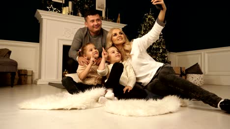 Family,-holidays,-technology-and-people---smiling-mother,-father-and-little-girls-making-selfie-with-camera-over-christmas-tree-lights-background