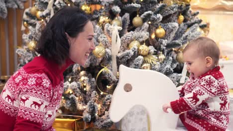 Mother-with-baby-girl-on-rocking-deer-toy-during-Christmas-eve