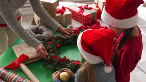 Zwei-Mädchen-in-Santa-Hüte-und-Frau-machen-Weihnachten-Kranz