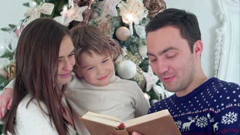 Joven-padre-leyendo-cuento-de-Navidad,-mientras-que-la-madre-y-su-hijo-feliz-susurrando-secretamente