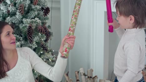 Happy-mother-and-son-having-wrapping-paper-sword-fight-near-the-Christmas-tree