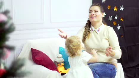 Happy-young-mother-playing-with-her-sweet-baby-in-a-decorated-room-near-the-christmas-tree