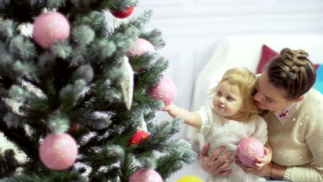 Happy-young-mother-playing-with-her-sweet-baby-in-a-decorated-room-near-the-christmas-tree