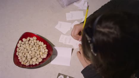 A-girl-sitting-at-a-kitchen-counter-drawing-on-pieces-of-paper,-with-snacks