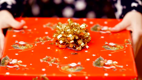 Close-up-of-two-child-hands-holding-a-Christmas-gift-in-a-beautiful-colored-paper-wrapper-with-a-gold-bow