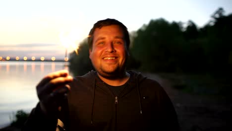 Portrait-of-young-smiling-man-with-sparkler-celebrating-at-beach-party