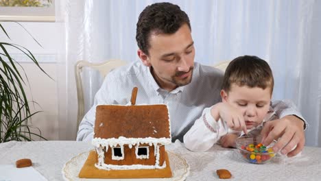 The-father-tells-how-decorate-a-gingerbread-house-to-a-little-son