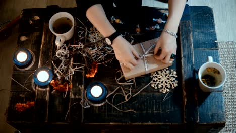 Top-view-of-female-hands-packing-a-holiday-present-for-friends.-Young-woman-decorating-the-Christmas-box-at-evening