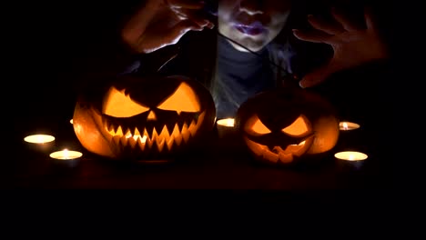 On-the-main-terms-of-the-pumpkin,-witch-casts-a-spell-from-behind..-Beautiful-young-woman-in-witches-hat-and-costume-holding-carved-pumpkin.-Halloween-art-design