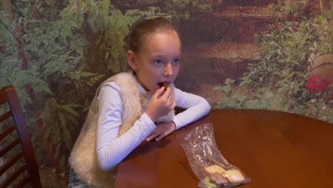 Joven-caucásica-sentado-en-la-mesa.-Joven-blanco-comiendo-galletas-de-jengibre-jengibre-y-viendo-la-televisión.-Joven-toma-el-desayuno-en-la-cocina-casera.-Desayuno-de-Navidad.-Mirando-a-la-cámara.