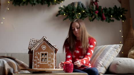 Beautiful-woman-wearing-winter-outfit-drinking-tea-with-gingerbread-at-home-near-Christmas-tree