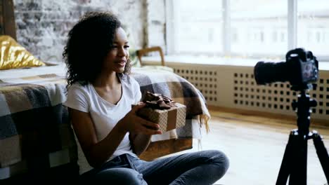 Atractiva-chica-africana-grabación-video-blog-sobre-embalaje-caja-de-regalo-de-Navidad-en-casa