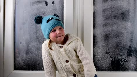 Small-girl-sits-on-windowsill-behind-the-frozen-window.