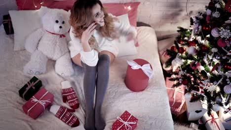 Junge-schöne-Frau-sitzt-auf-einem-Bett-mit-Teddy-Bär-in-der-Nähe-von-einem-Weihnachtsbaum-und-spricht-am-Telefon.-Ansicht-von-oben.