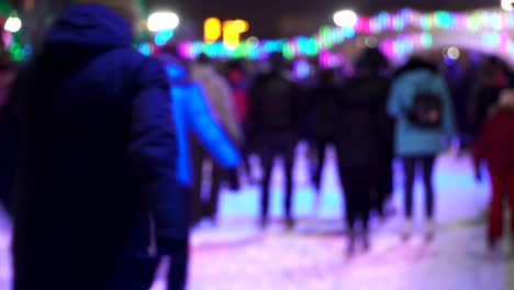 Deporte-de-invierno-de-concepto.-Multitud-en-la-ciudad-de-patinaje-la-noche-pista.-Gran-multitud-de-personas-alegres-que-se-divierten-patinando.-Nieve-que-cae.-Desenfoque-de-días-de-Navidad.-Deporte-y-buen-humor-concepción.-Familias-y-feliz-pareja-patinaje