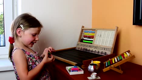 Sweet-little-girl-plays-with-abacus-and-writes-on-blackboard-with-chalk.-Preschool-concept,-childhood-concept.-Toy-abacus-with-Czech-alphabet.-Cute-girl-like-preschooler