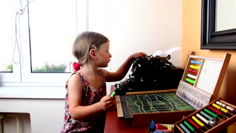 Sweet-little-girl-plays-with-abacus-and-writes-on-blackboard-with-chalk.-Preschool-concept,-childhood-concept.-Toy-abacus-with-Czech-alphabet-and-vintage-typewriter.-Cute-girl-like-preschooler