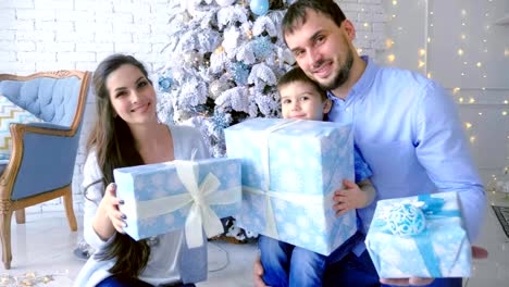 Happy-family,-mom-dad-son,-pile-up-boxes-with-gifts-up.-Christmas-background.