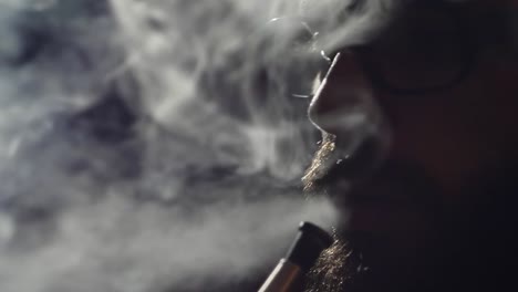 young-bearded-man-in-glasses-smokes-a-hookah-and-blow-out-smoke-closeup-on-black-background-in-slow-motion-in-4k