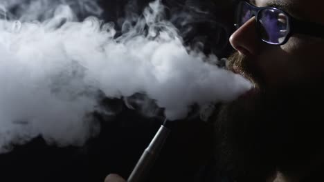 young-bearded-man-in-glasses-smokes-a-hookah-and-blow-out-smoke-closeup-on-black-background-in-slow-motion-in-4k