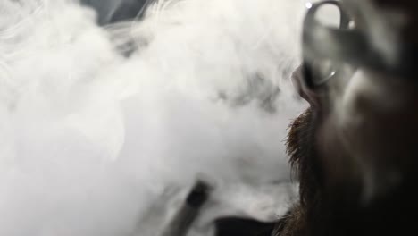 young-bearded-man-in-glasses-smokes-a-hookah-and-blow-out-smoke-closeup-on-black-background-in-slow-motion-in-4k