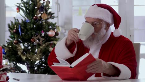 Santa-Claus-ist-aus-einer-Tasse-trinken-und-ein-Buch-zu-lesen