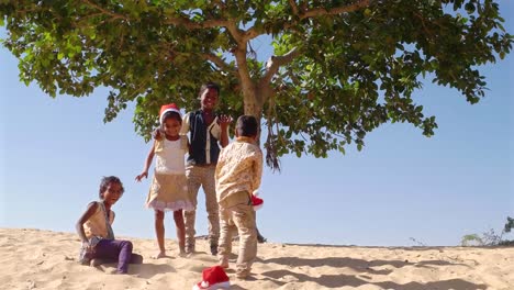 WS-Kinder-umarmt-umarmt-und-kauern-in-Sand-der-Wüste-mit-Santa-Hüte-unter-einem-Baum