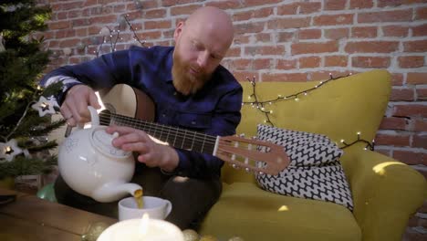 Man-with-guitar-sitting-next-to-Christmas-tree-and-pouring-tea