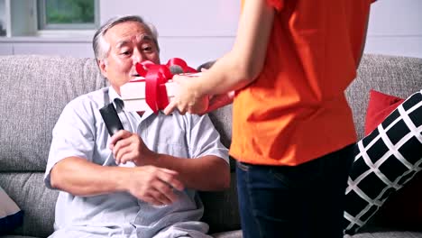 I-got-a-present-for-you.-Daughter-giving-her-senior-father-a-surprise-present.-Asian-man-with-white-beard-and-beautiful-woman.-Senior-lifestyle-concept.