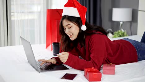 glückliche-Frau-online-shopping-für-Weihnachtsgeschenk-mit-Computer-Laptop-und-Kreditkarte-auf-einem-Bett