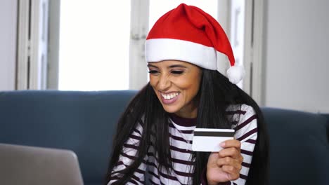 Woman-wearing-red-sweater-and-santa-claus-hat-holding-credit-card-choosing-and-buying-christmas-gifts-using-laptop-at-home-excited-with-internet-sales-and-credit-card-facilities-in-on-line-shopping