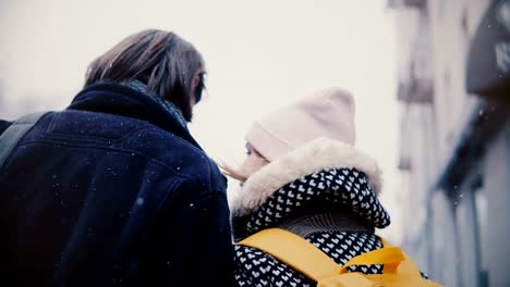 Back-view-happy-relaxed-young-romantic-couple-in-casual-warm-clothes-walk-together-and-kiss-on-a-snowy-cold-winter-day.