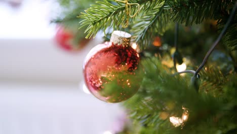 Mano,-profundidad-de-campo-cerca-de-chucherías-brillantes-colgando-de-un-árbol-de-Navidad-con-luces