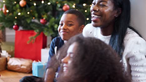 Aufgeregten-Kinder-sitzen-am-Boden-mit-Mutter-als-Familie-gemeinsam-Weihnachten-feiern