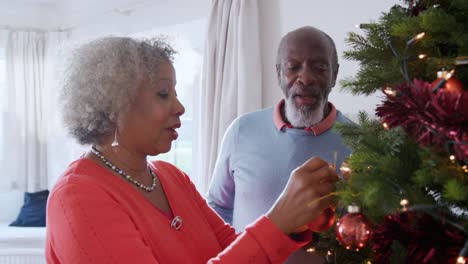 Älteres-paar-hängende-Dekoration-am-Weihnachtsbaum-zu-Hause-zusammen