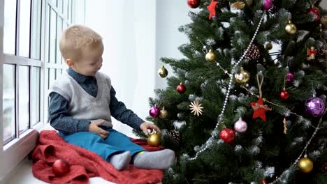 Little-baby-boy-decorating-a-Christmas-tree-toys.-Holidays,-gift,-and-new-year-concept