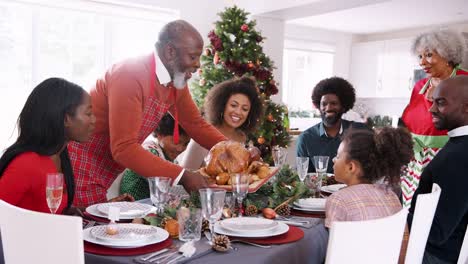 Abuelo-que-un-pavo-asado-a-la-mesa-durante-una-generación-multi,-mezclado-raza-celebración-familiar-de-Navidad