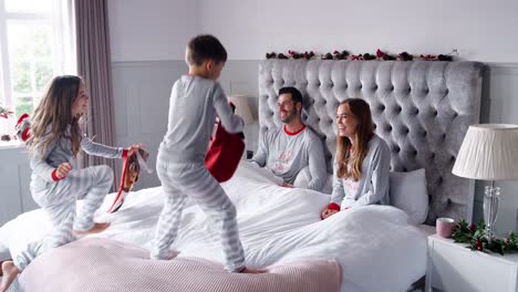 Begeistert-Kinder-laufen-ins-Schlafzimmer-der-Eltern-zu-Hause-mit-Strümpfen-und-Prellen-auf-Bett-als-Familie-öffnen-Geschenke-am-ersten-Weihnachtstag