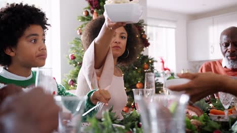 Vista-de-ángulo-bajo-de-multi-generación-negro-familia-comer-pasando-unos-a-otros-alimentos-en-su-mesa-de-Navidad