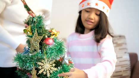 Feliz-niña-asiática-decorando-un-árbol-de-Navidad-con-su-madre