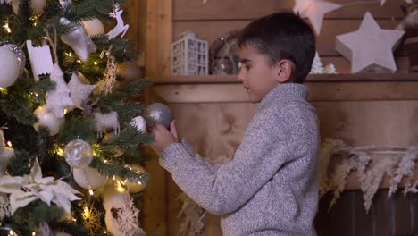 Ein-kleiner-Junge-schmückt-einen-Weihnachtsbaum-mit-einem-schönen-Ball-mit-einer-guten-Stimmung.