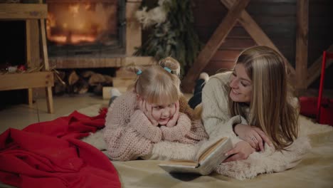 Merry-Christmas-and-Happy-New-Year.-Beautiful-family-in-Xmas-interior.-Pretty-young-mother-reading-a-book-to-her-daughter-near-Christmas-tree