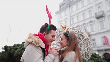 Schönes-paar-stehen-auf-der-Straße-und-Verschleiß-Weihnachten-Hörner-am-Kopf.-Lächeln-Sie,-um-Kamera-und-geben-eine-Umarmung-zu