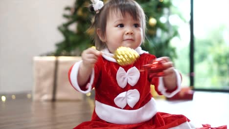 Niedliche-1-Jahr-alt-Baby-Mädchen-tragen-Rentier-Haarreif-mit-Christbaumkugel-mit-Weihnachtsbaum-im-Hintergrund-zu-spielen.-Frohe-Weihnachten-und-schöne-Feiertage!