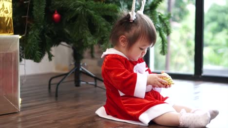 Cute-1-year-old-baby-girl-wearing-reindeer-headband-playing-with-Christmas-ornament-with-christmas-tree-in-background.-Merry-Christmas-and-Happy-Holidays!