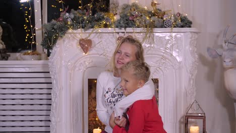 Smiling-sister-hugging-little-brother-on-Christmas-fireplace-background