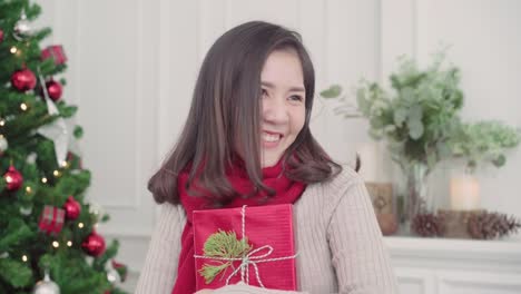 Alegre-feliz-joven-mujer-asiática-con-regalos-de-Navidad-sonriendo-a-la-cámara-en-su-sala-de-estar-en-el-país-en-el-Festival-de-Navidad.-Mujer-de-estilo-de-vida-celebrar-Navidad-y-año-nuevo-concepto.