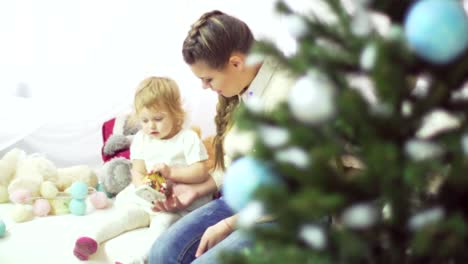 Happy-young-mother-playing-with-her-sweet-baby-in-a-decorated-room-near-the-christmas-tree